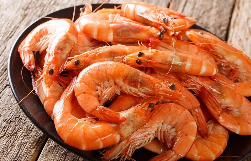 Nahaufnahme eines schwarzen Tellers mit ungeschälten Garnelen auf grobem Holzuntergrund.