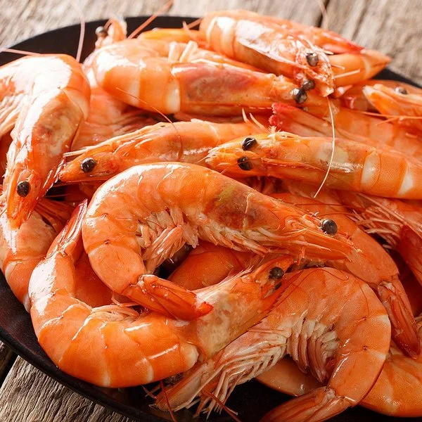 Nahaufnahme eines schwarzen Tellers mit ungeschälten Garnelen auf grobem Holzuntergrund.