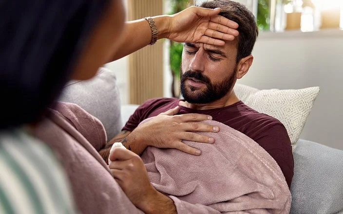 Eine Frau fasst einem Mann an die Stirn und prüft, ob er Fieber hat.