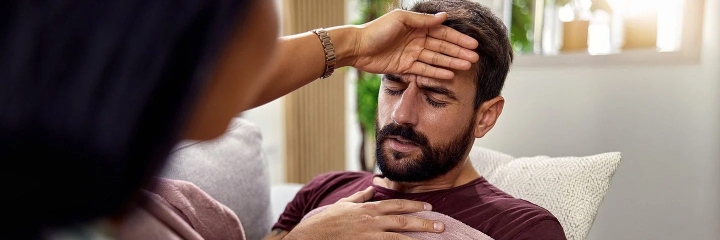 Eine Frau fasst einem Mann an die Stirn und prüft, ob er Fieber hat.