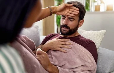 Eine Frau fasst einem Mann an die Stirn und prüft, ob er Fieber hat.