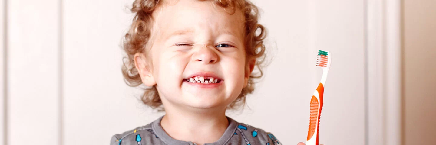 Ein Junge mit Zahnlücke zeigt seine Zähne und eine Zahnbürste.