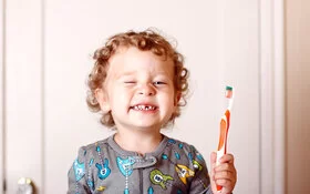 Ein Junge mit Zahnlücke zeigt seine Zähne und eine Zahnbürste.