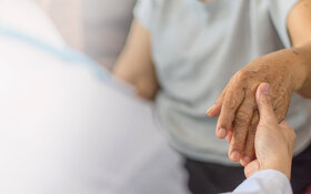 Ein Arzt untersucht eine ältere Patientin mit Parkinson und hält ihre Hand.