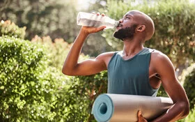 Ein junger Mann trinkt nach dem Sport im Freien aus einer Glasflasche Wasser.