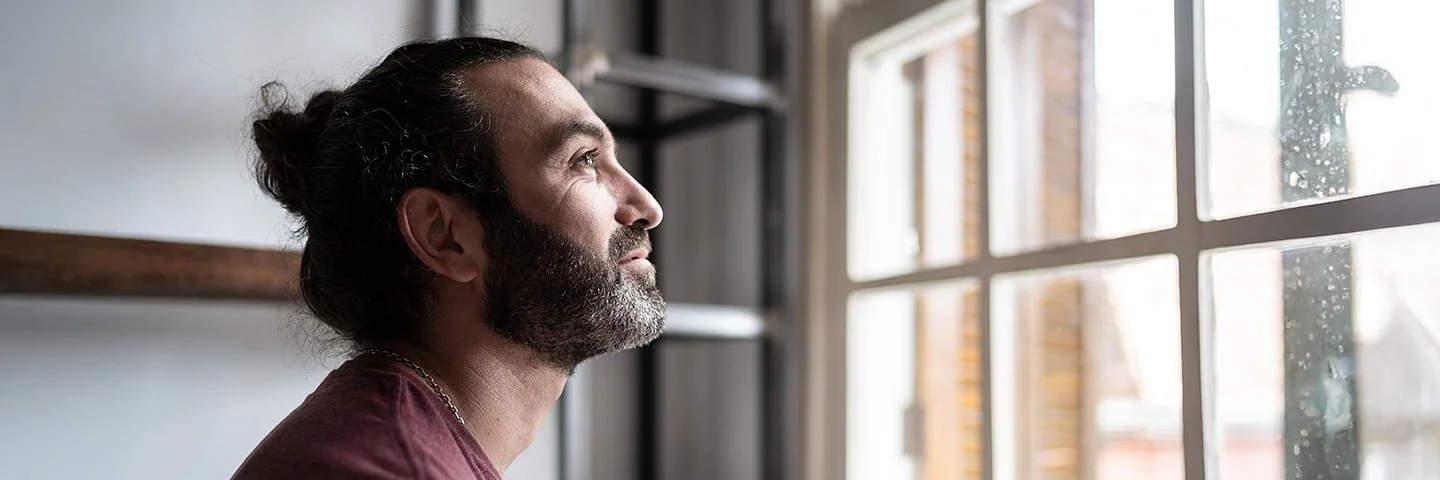Ein Mann befindet sich in einem Innenraum und schaut aus einem Fenster. Er lächelt.