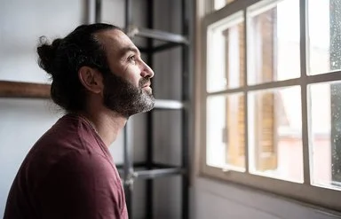 Ein Mann befindet sich in einem Innenraum und schaut aus einem Fenster. Er lächelt.
