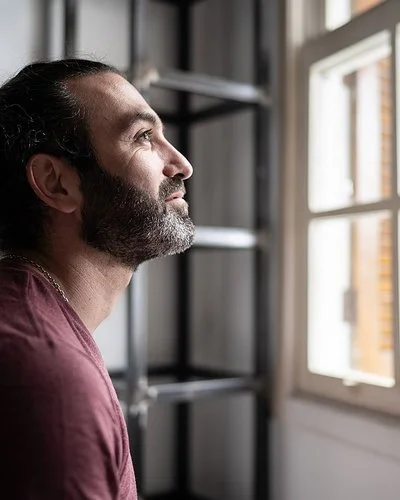 Ein Mann befindet sich in einem Innenraum und schaut aus einem Fenster. Er lächelt.