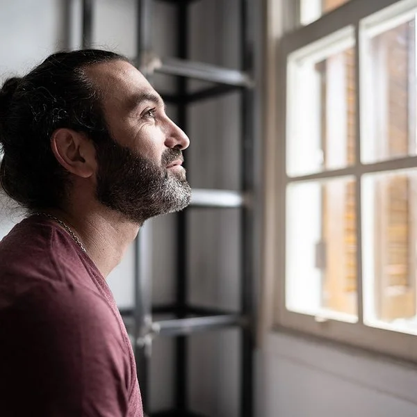 Ein Mann befindet sich in einem Innenraum und schaut aus einem Fenster. Er lächelt.