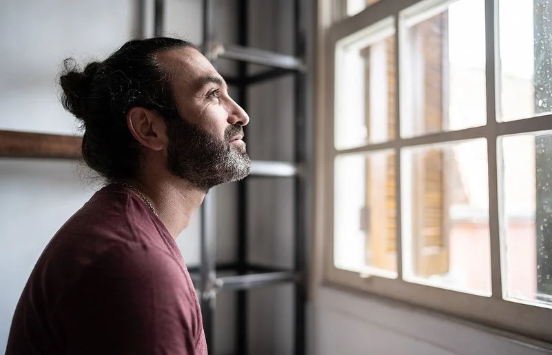 Ein Mann befindet sich in einem Innenraum und schaut aus einem Fenster. Er lächelt.