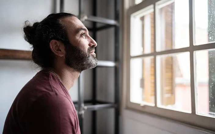 Ein Mann befindet sich in einem Innenraum und schaut aus einem Fenster. Er lächelt.