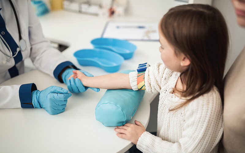 Eine Ärztin bereitet in ihrer Praxis den Arm eines kleinen Mädchens für eine Blutentnahme vor.
