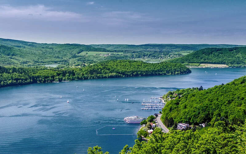 Panorama des Edersees in Hessen: bewaldete Hügel, Segelboote und ein kleiner Yachthafen am Ufer.