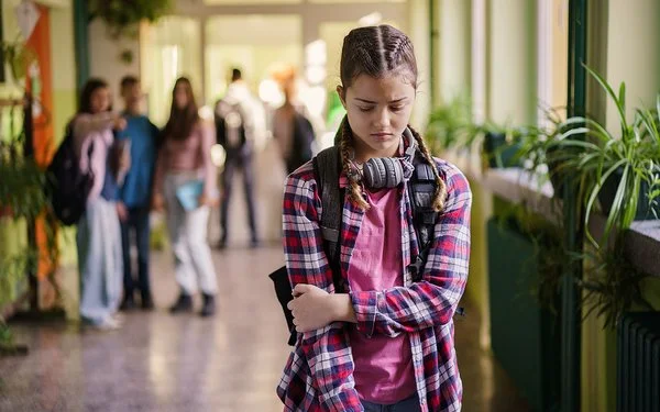Ein Mädchen im Teenager-Alter steht mit gesenktem Blick auf einem Schulflur.