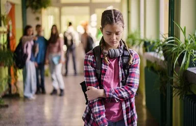 Ein Mädchen im Teenager-Alter steht mit gesenktem Blick auf einem Schulflur.