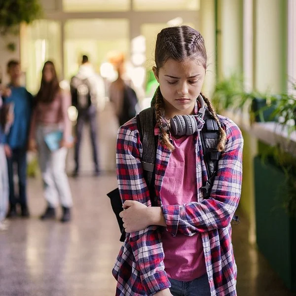 Ein Mädchen im Teenager-Alter steht mit gesenktem Blick auf einem Schulflur.