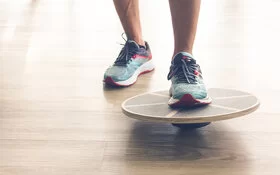 Nahaufnahme von einen Fuß mit Sportschuh, der auf ein rundes Balance Board tritt.