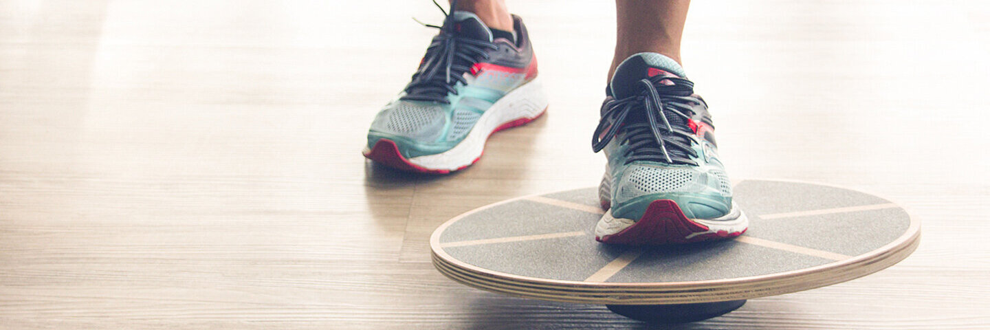 Nahaufnahme von einen Fuß mit Sportschuh, der auf ein rundes Balance Board tritt.