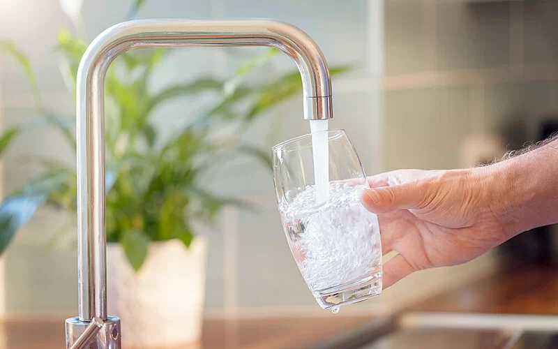 Ein Mann hält ein Glas unter einen Wasserhahn und füllt es.