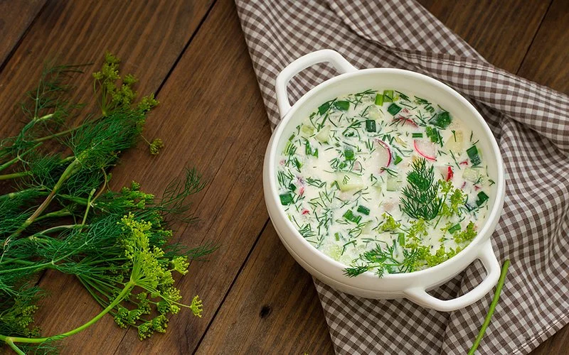 Eine Schüssel mit einer hellen Dill-Suppe steht auf einem Holztisch.
