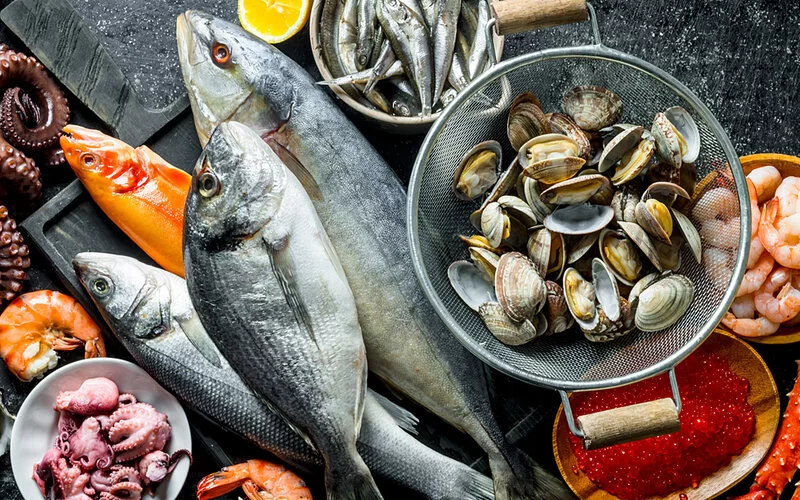 Eine Zusammenstellung verschiedener Seefische und Tintenfische sowie Muscheln, Krustentiere und Fischrogen auf Schieferplatten.