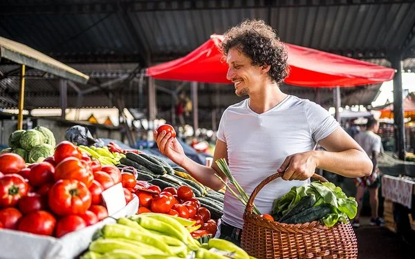 Ein Mann kauft mit einem Weidenkorb in der Hand auf dem Markt ein.