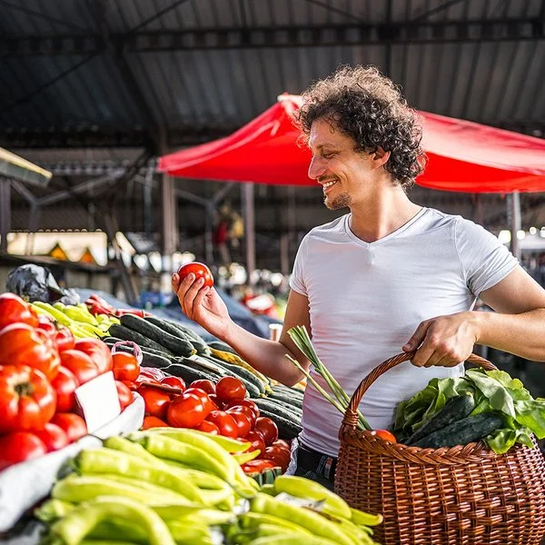 Ein Mann kauft mit einem Weidenkorb in der Hand auf dem Markt ein.