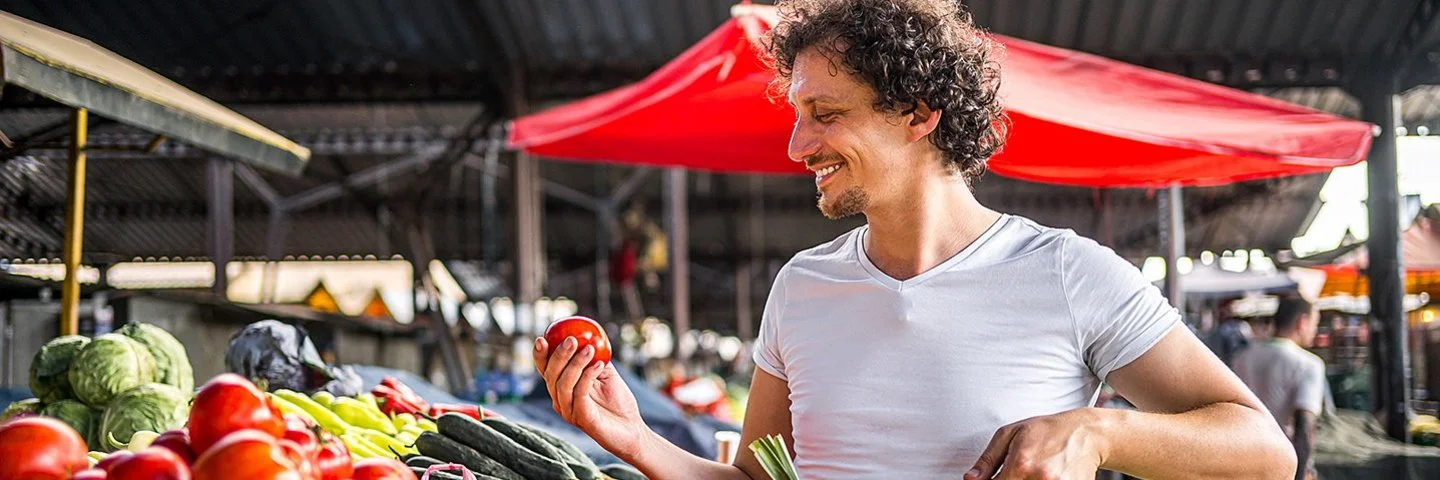 Ein Mann kauft mit einem Weidenkorb in der Hand auf dem Markt ein.