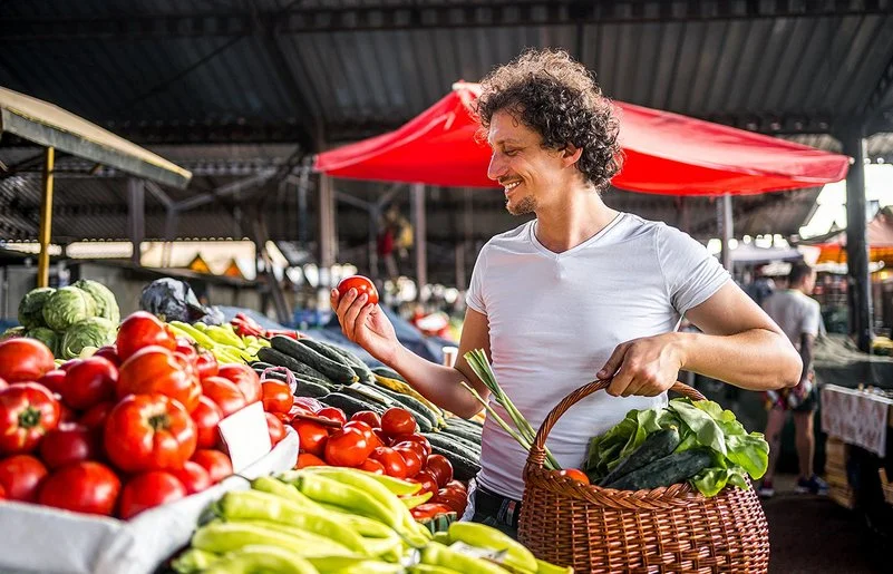 Ein Mann kauft mit einem Weidenkorb in der Hand auf dem Markt ein.