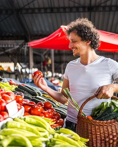 Ein Mann kauft mit einem Weidenkorb in der Hand auf dem Markt ein.