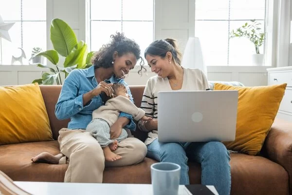 Junges Paar sitzt mit einem Laptop und einem Kind auf dem Sofa