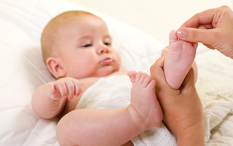 Eine erwachsene Preson massiert die Füße eines Babys.