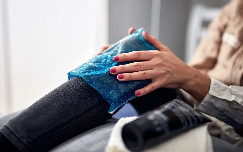 Eine Frau hält mit den Händen ein kaltes Gel-Pad auf dem rechten Knie.