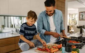 Vater und Sohn kochen zusammen in der Küche mit gesunden Lebensmitteln.