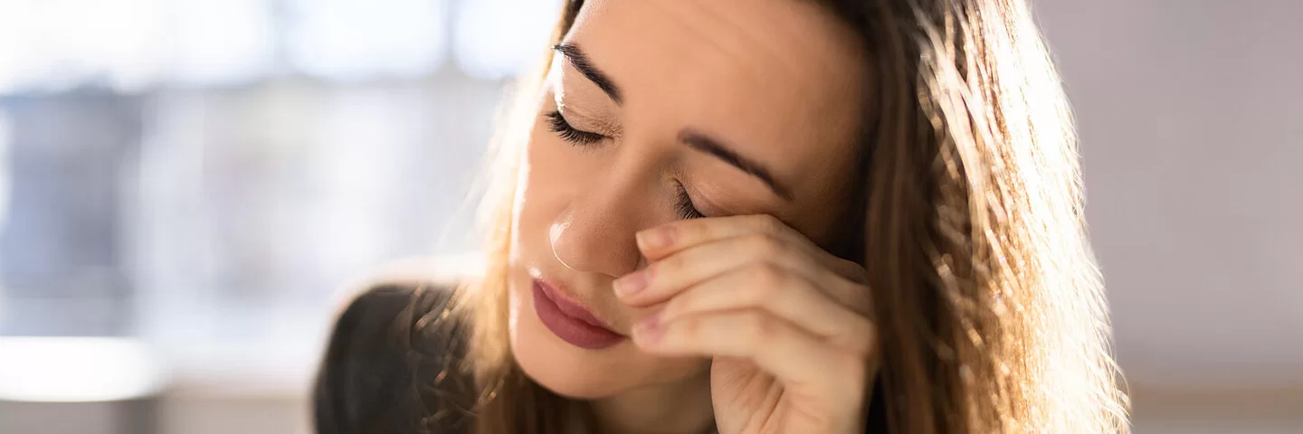 Eine junge Frau mit geschlossenen Augen reibt sich das linke Auge.