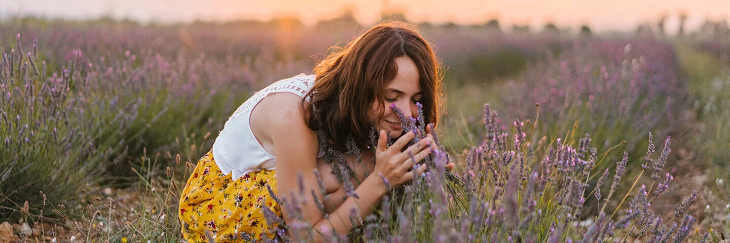 Eine Frau steht in einem Feld mit Lavendel und riecht an den Blüten.