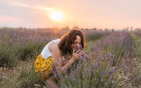 Eine Frau steht in einem Feld mit Lavendel und riecht an den Blüten.
