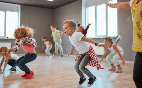 Eine Gruppe von kleinen Mädchen und Jungen springt und tanzt im Tanzunterricht.