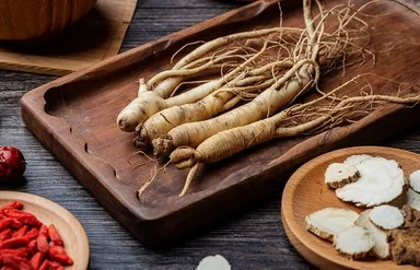 Vier Ginsengwurzeln liegen nebeneinander auf einem hölzernen Tablett.