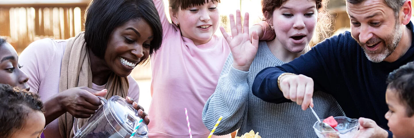 Eine Patchworkfamilie sitzt an einem Tisch mit mitgebrachten Speisen und Getränken.