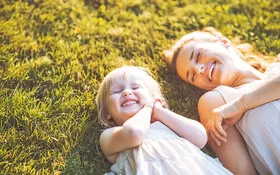 Junge Mutter mit Tochter liegen auf einer Wiese und tanken Vitamin D beim Sonnenbaden.