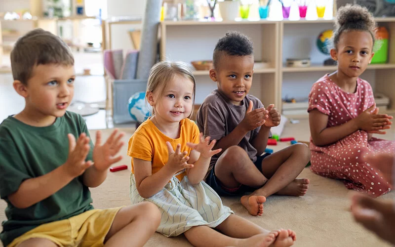Kinder verschiedener Herkunft sitzen im Kindergarten gemeinsam auf dem Boden und sind vergnügt.