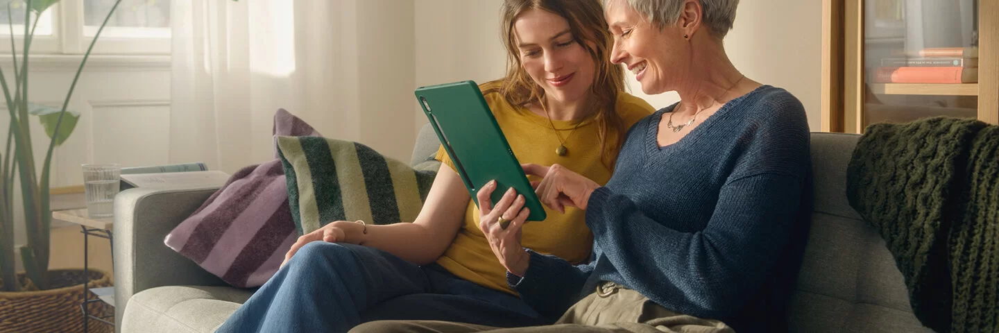2 Frauen sitzen auf der Couch und schauen gemeinsam auf ein Tablet
