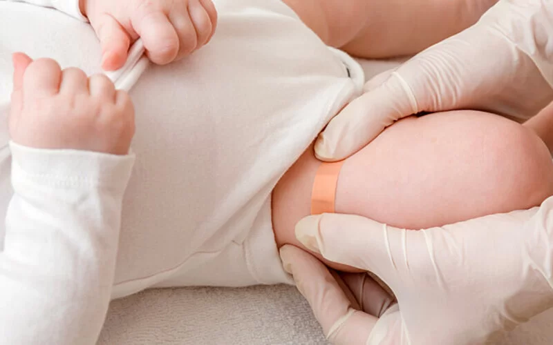 Ein Arzt klebt einem Baby ein Pflaster nach dem Impfen aufs Bein.