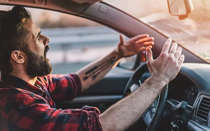 Junger Mann sitzt gereizt im Auto und regt sich über andere Fahrer auf.