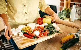Jemand trägt ein Brett mit frischen Lebensmitteln in die Küche, um für sich gesund zu kochen.