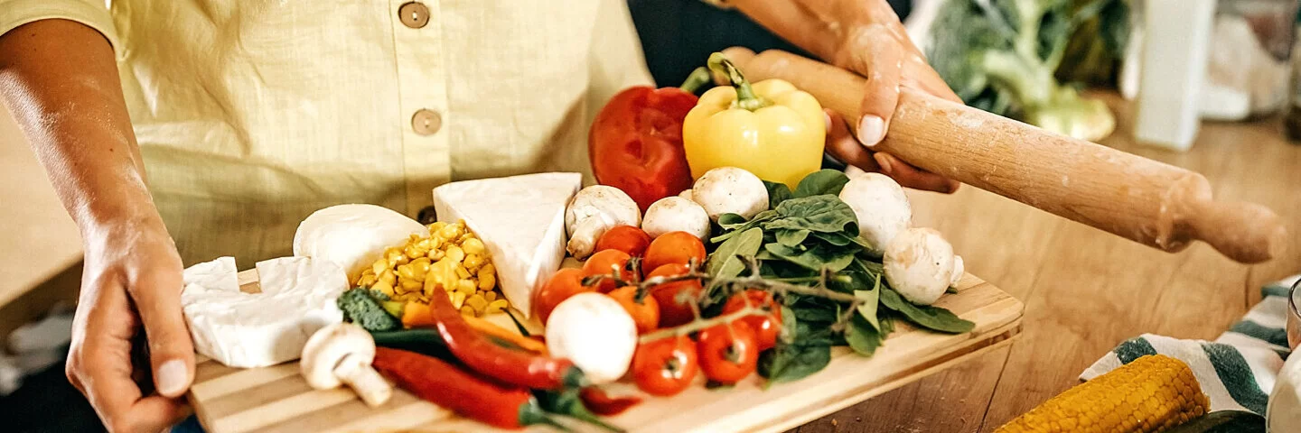 Jemand trägt ein Brett mit frischen Lebensmitteln in die Küche, um für sich gesund zu kochen.