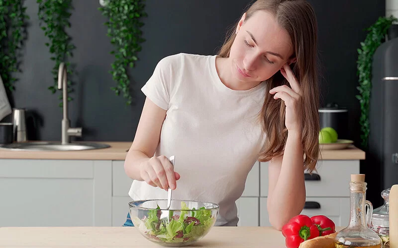 Junges, schlankes Mädchen stochert lustlos in ihrem Salat herum und mag kaum etwas essen, vielleicht ist sie von Magersucht betroffen.