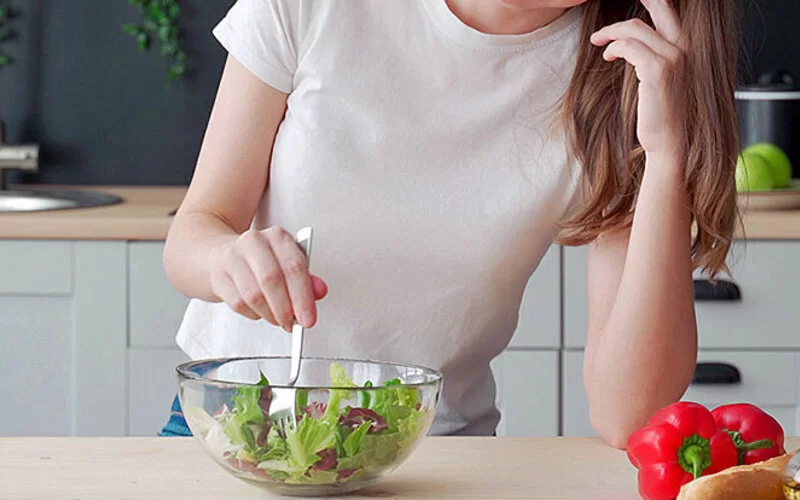 Junges, schlankes Mädchen stochert lustlos in ihrem Salat herum und mag kaum etwas essen, vielleicht ist sie von Magersucht betroffen.