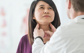 Ein Arzt untersucht mit den Händen die Schilddrüse einer jungen Frau.